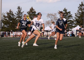 A women's lacrosse player in a white Northwestern jersey runs in front of two other players in Penn State jerseys