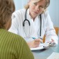 A doctor looks at a patient as if to listen to reported symptoms.