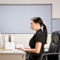 A woman sits at a desk typing on a computer.
