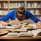 a student struggles with homework, sleeping on a pile of books