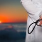 A doctor's hands are shown to be holding a stethoscope with a background of a sunset behind him or her.