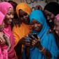 Girls in head coverings gather around one who is holding a cell phone