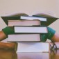 Someone sits behind a stack of textbooks