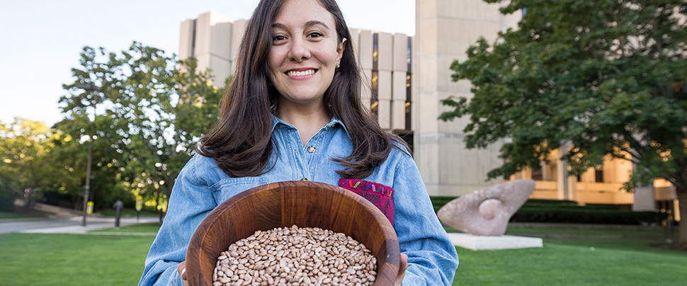 Odette Zero holding a bowl of beans in front of University Library.