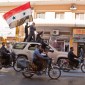 A man in an SUV holds a Syrian flag while the SUV drives. 