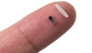 Pacemaker next to a single grain of rice on a fingertip.