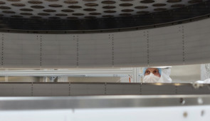 A researcher in protective gear peers through two cylindrical scientific instruments
