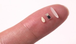 Tiny pacemaker on a fingertip, between a sesame seed and single grain of rice for scale.