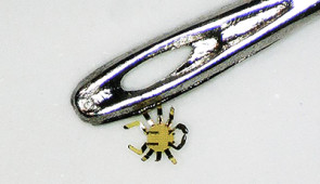 Smaller than a flea, tiny robotic crab sits next to the eye of a sewing needle.
