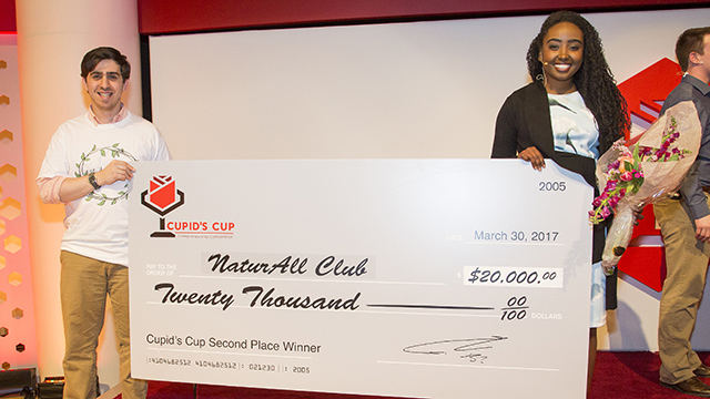 Two people, a man and a woman, hold a large check made out to NaturAll Club for $20,000.