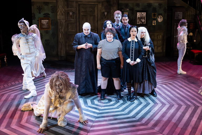 Actors playing the Addams Family pose centerstage while ringed by three dancers 