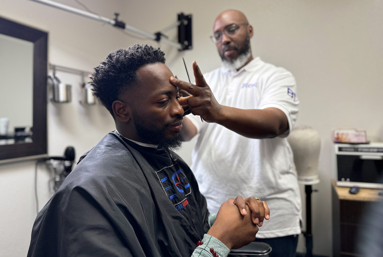 Dr. Keven Stonewall sits in a chair to receive a haircut from his barber, Dorrian “Dee” Whigham