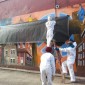 Three people wearing white painter suits cover up a mural with a tarp.