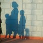 The shadows of three people fall on a cinderblock wall.