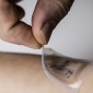 A hand peels a translucent electronic patch from an arm.