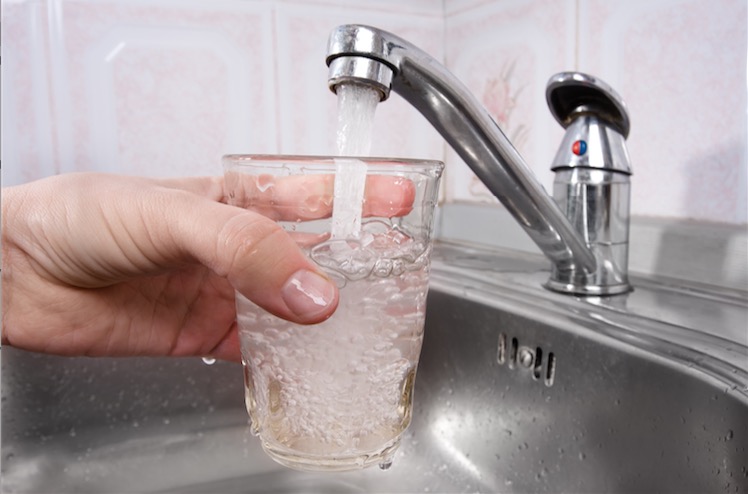 A hand holds a glass under a water faucet