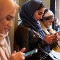 Women dressed in head-scarves check their phones.