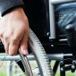 A man's hand grips the rail on a wheelchair