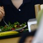 A hand holds a fork touching a salad on a plate.