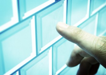 An index finger touches a touchscreen displaying blue blocks that resemble a computer keyboard