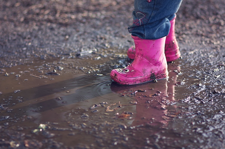 A child wearing pink rain boots standing in a mud puddle