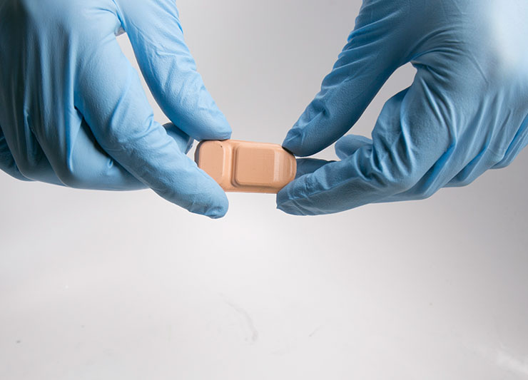 Blue-gloved hands holding bandage-like sensor