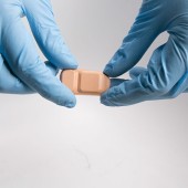 Blue-gloved hands holding bandage-like sensor