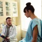 A transgender woman in a hospital gown speaking to her doctor, a transgender man, in an exam room
