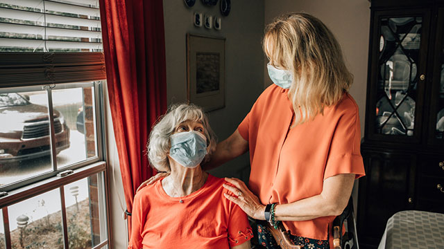 Two women, one seated one standing, wearing masks