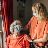 Two women, one seated one standing, wearing masks