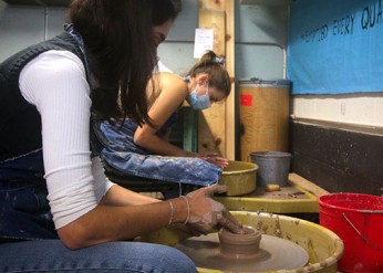 Two students molding clay on a pottery wheel