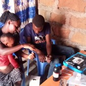 A woman seated with baby on her lap and her husband conduct a water quality test at home