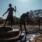 Two men collect water from a well. There are sevarl camels in the background.