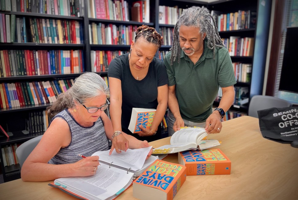 surrouned by bookshelves, three people look at a book manuscript and the novel "Divine Days" 