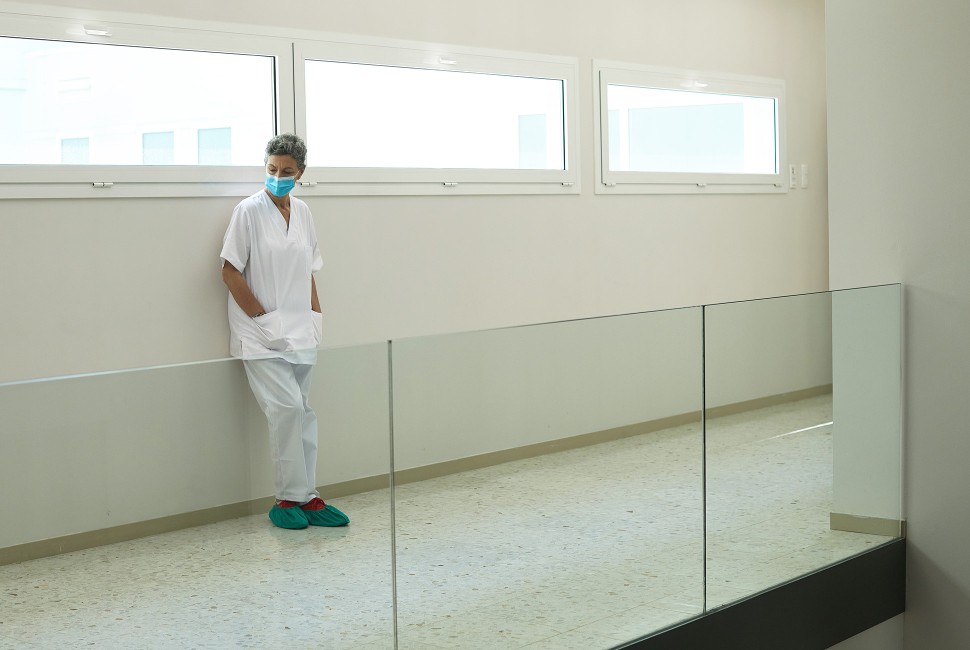 A healthcare worker leans against a wall in an empty corridor