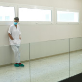 A healthcare worker leans against a wall in an empty corridor
