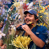 A birdwatcher with binoculars surrounded by wildflowers
