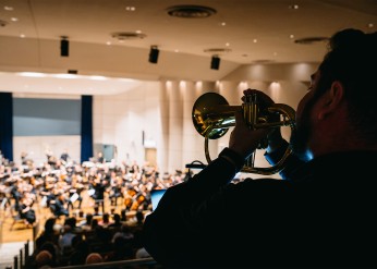 In the foreground, a musician plays the flugelhorn toward an orchestra onstage