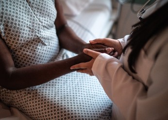 A doctor holds a Black patient's hands 