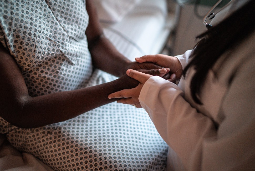 A doctor holds a Black patient's hands 