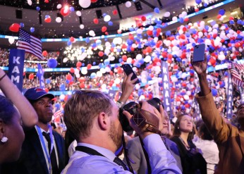 A student takes photographs during the DNC as balloons fall from the ceiling of the United Center