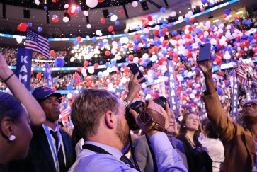 A student takes photographs during the DNC as balloons fall from the ceiling of the United Center