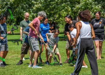 Adults and children play lacrosse outside