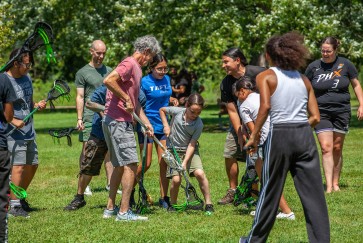 Adults and children play lacrosse outside