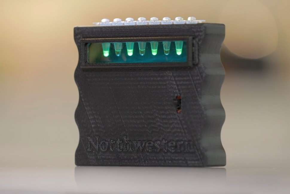 A small black device contains test tubes that glow green