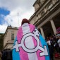 A person wearing a trans flag emblazoned with the gender inclusivity symbol