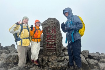 Three hikers pose on the summit of a mountain