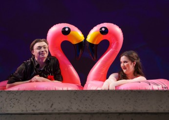 two performers sit on inflatable flamingos