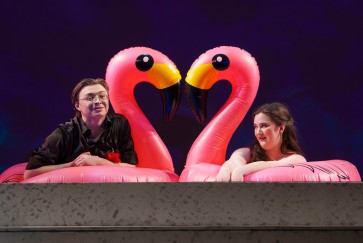 two performers sit on inflatable flamingos