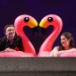 two performers sit on inflatable flamingos